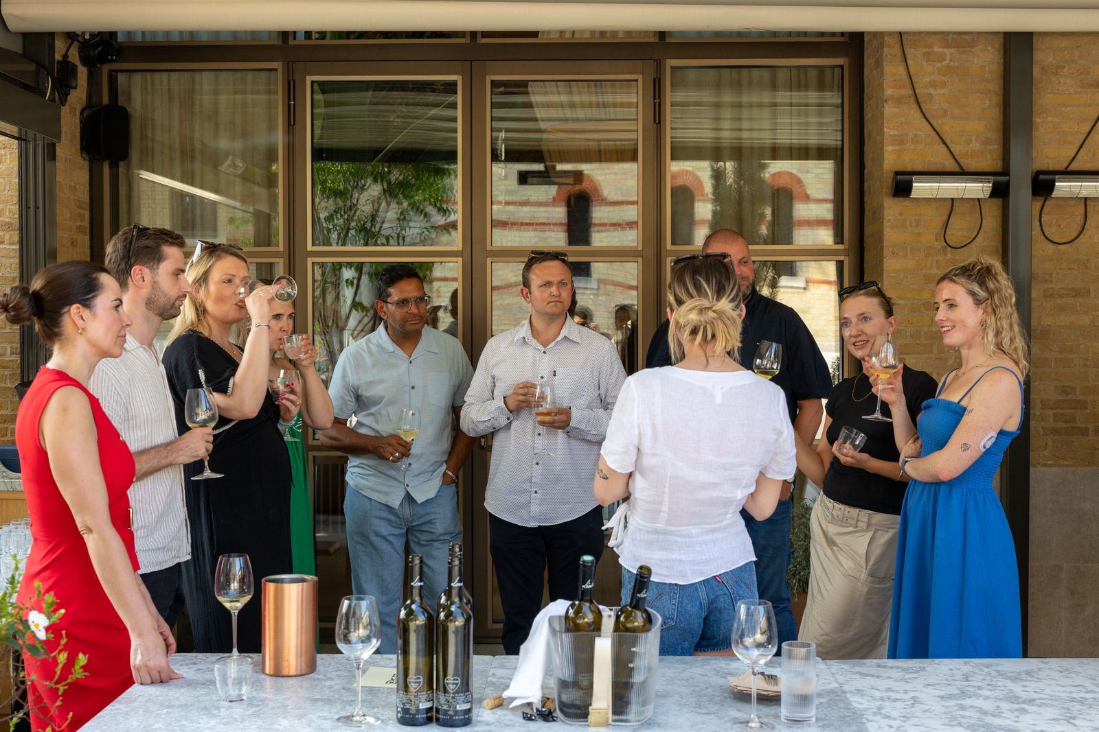 Sunlit indoor dining space with patterned benches, wooden tables, and an olive tree surrounded by lush greenery