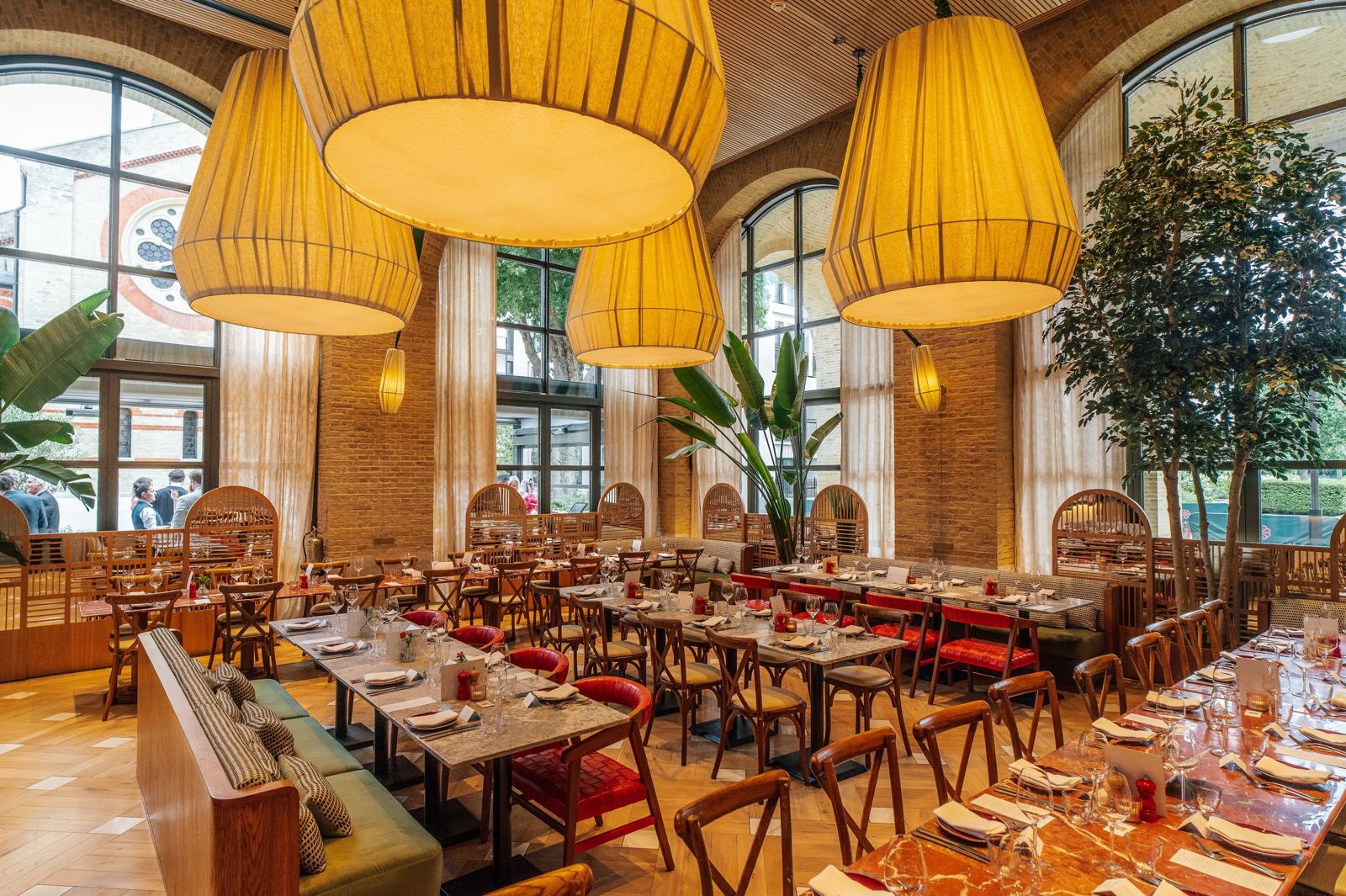 Outdoor dining tables with red chairs and marble tops, set with glassware and flowers, ready for service in the sun
