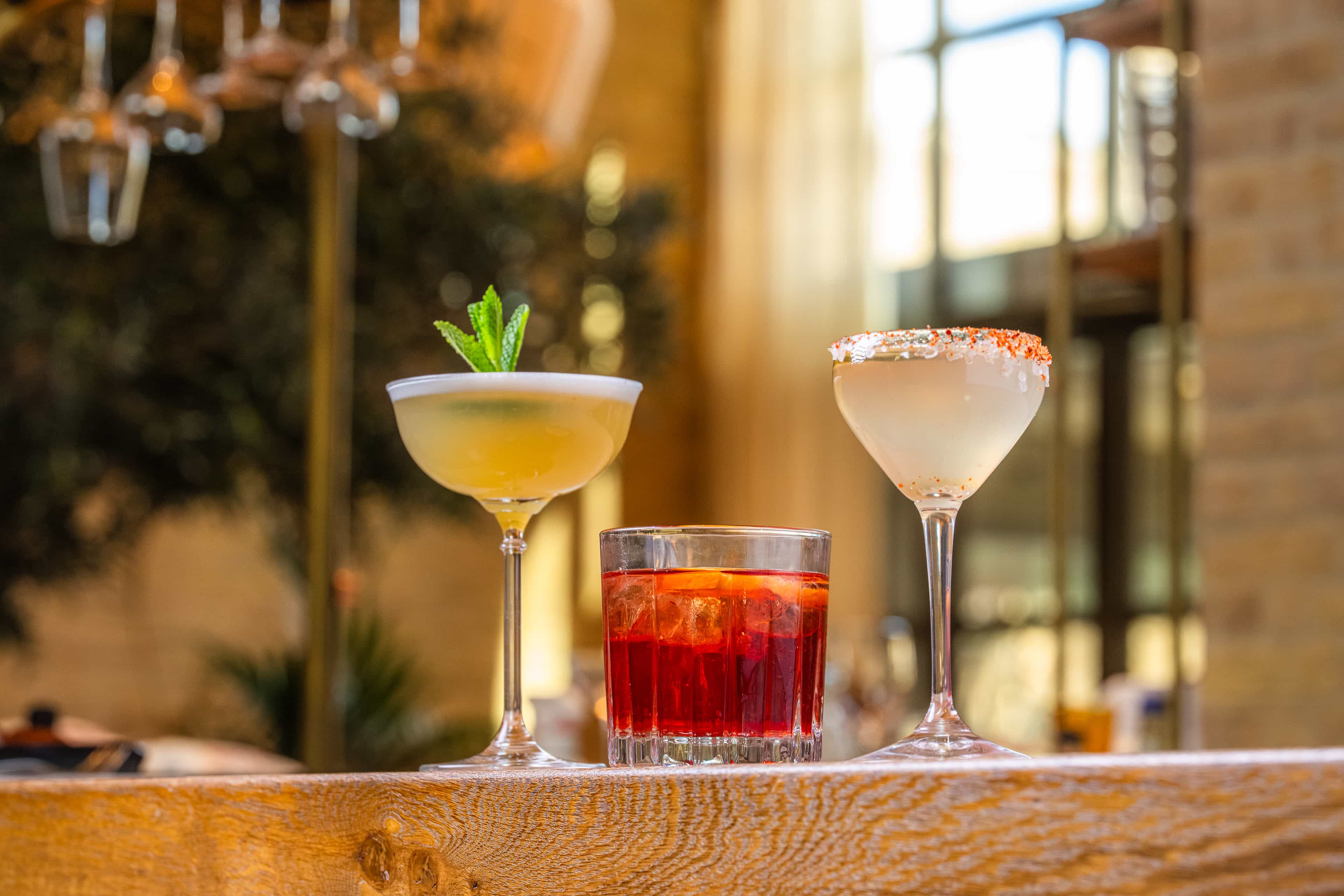 Glass and pitcher of red sangria with citrus slices and ice, next to a small vase with fresh flowers