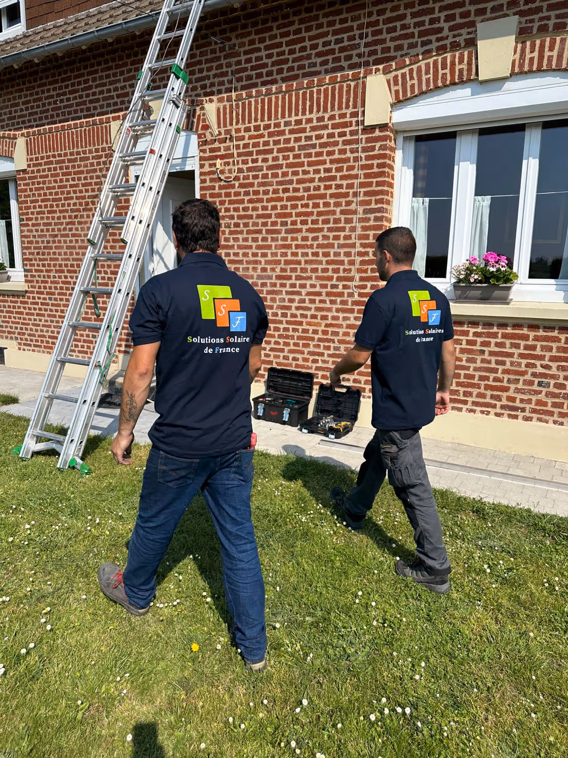 Deux hommes debout sur une échelle devant un bâtiment en briques.
