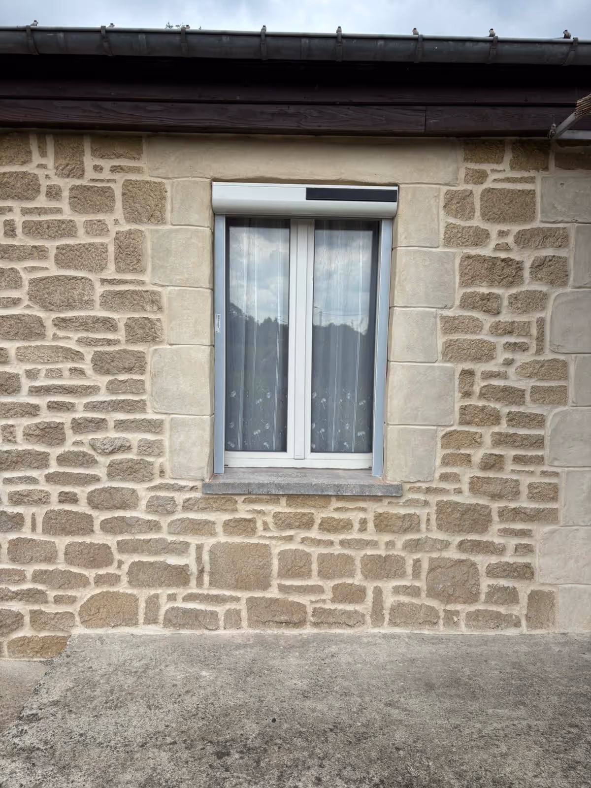 petite fenêtre équipée d'un volet roulant solaire sur un mur en pierre