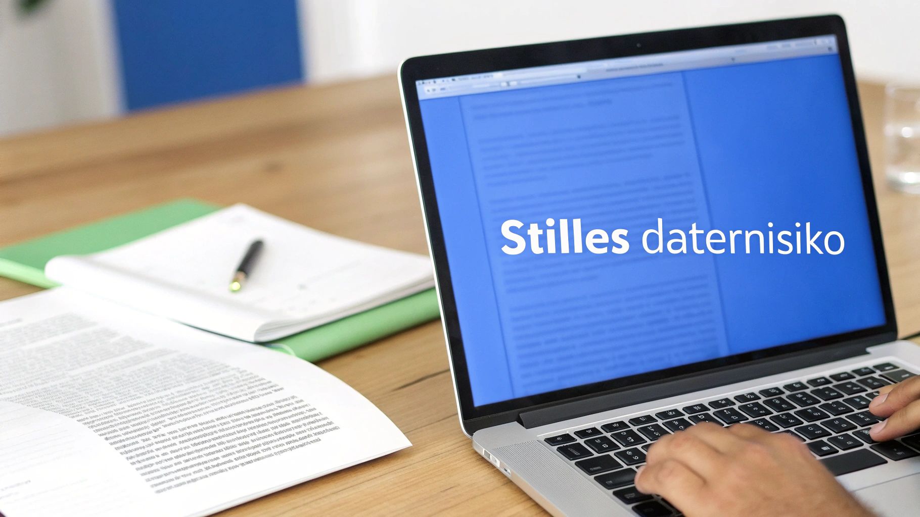 Eine Person tippt auf einem Laptop mit der Überschrift 'Stilles daternisiko' auf dem Bildschirm. Auf dem Schreibtisch liegen Dokumente und ein Notizbuch.