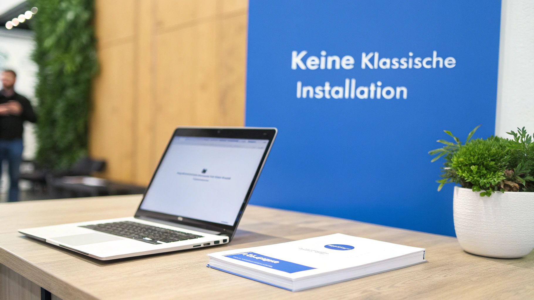 Laptop, Buch und Pflanze auf einem Schreibtisch vor einer blauen Wand mit der Aufschrift 'Keine Klassische Installation'.