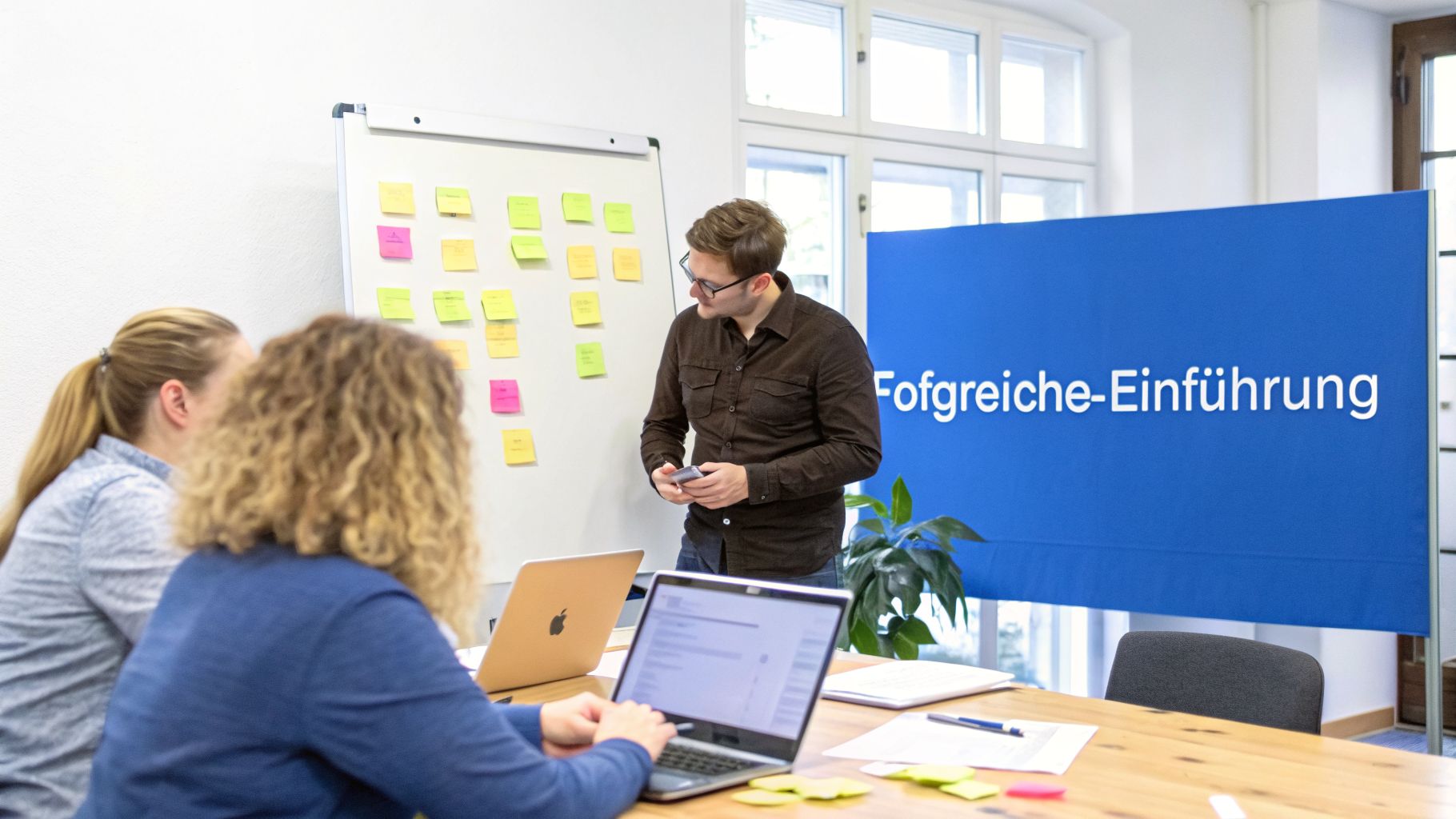 Ein Team arbeitet in einem hellen Büro, diskutiert Ideen am Whiteboard mit Haftnotizen und arbeitet an Laptops.