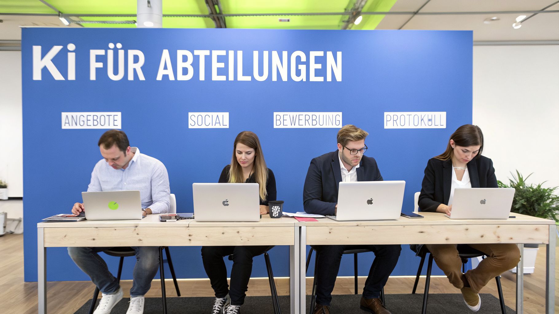 Vier Personen arbeiten konzentriert an Laptops an einem Stand mit blauer Rückwand und deutscher Beschriftung.
