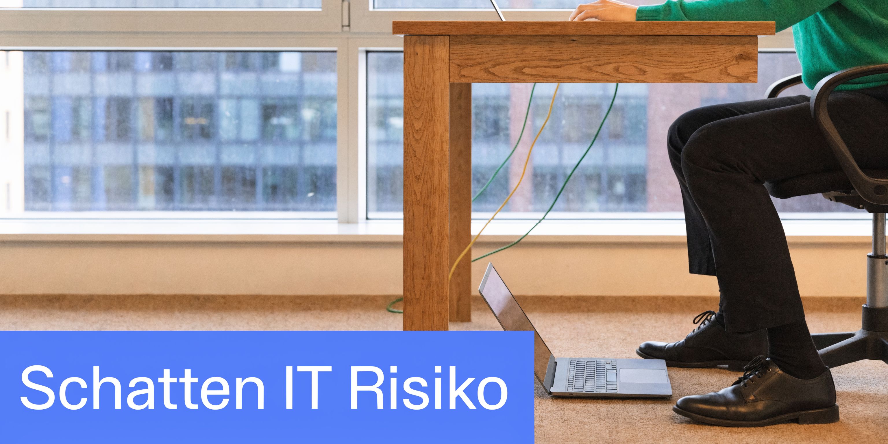 Ein Mitarbeiter arbeitet im Büro an einem Schreibtisch mit zwei Laptops und Kabeln am Boden.