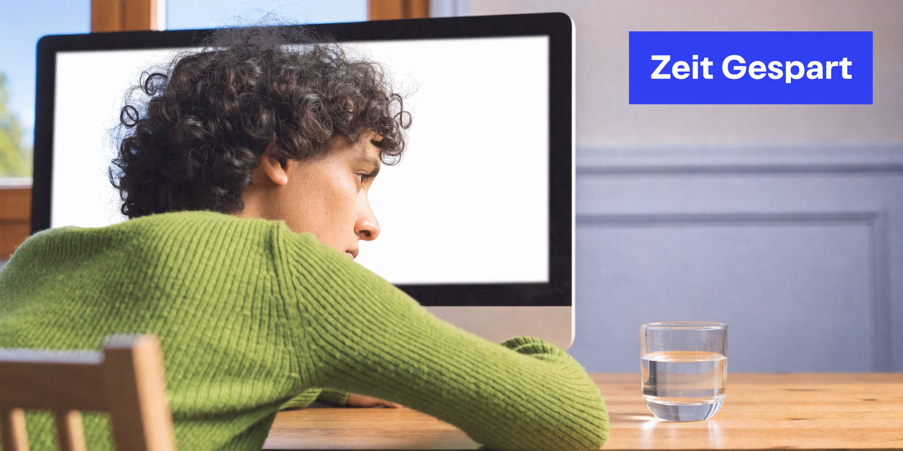 Ein nachdenklicher junger Mann starrt auf einen leeren Computerbildschirm, während er an einem Holztisch mit einem Wasserglas sitzt.