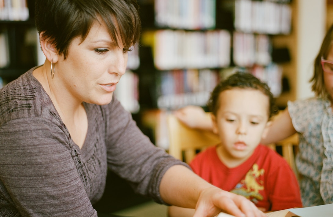 A female hollam private teacher sitting at a table with a young student.