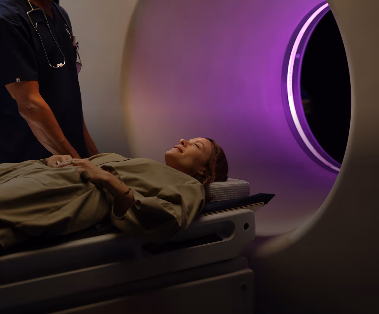 Patient lying on a hospital bed being guided into an MRI scanner emitting purple light.