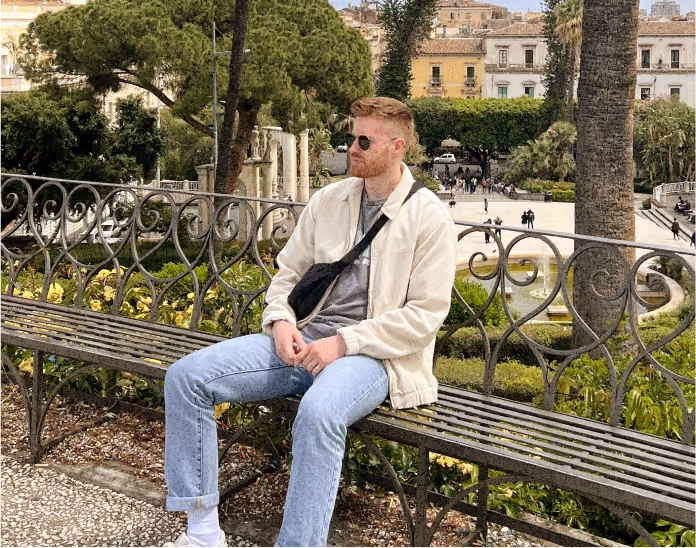 Simon sat on a bench in front a picturesque park in Sicily