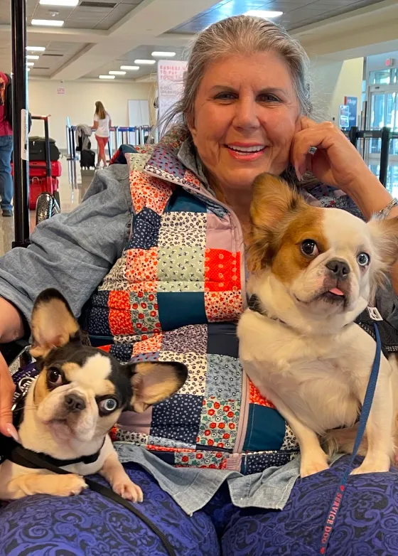 Anahata Graceland sitting in an airport with two Regular Royal Frenchel service dogs.