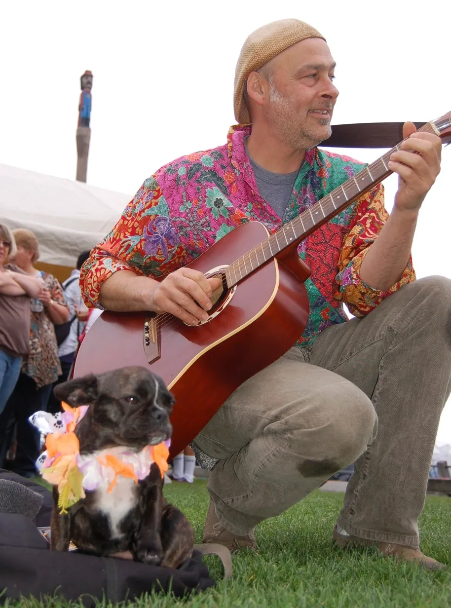 Super Micro Royal Frenchel companion sitting calmly in a park beside its owner playing guitar.