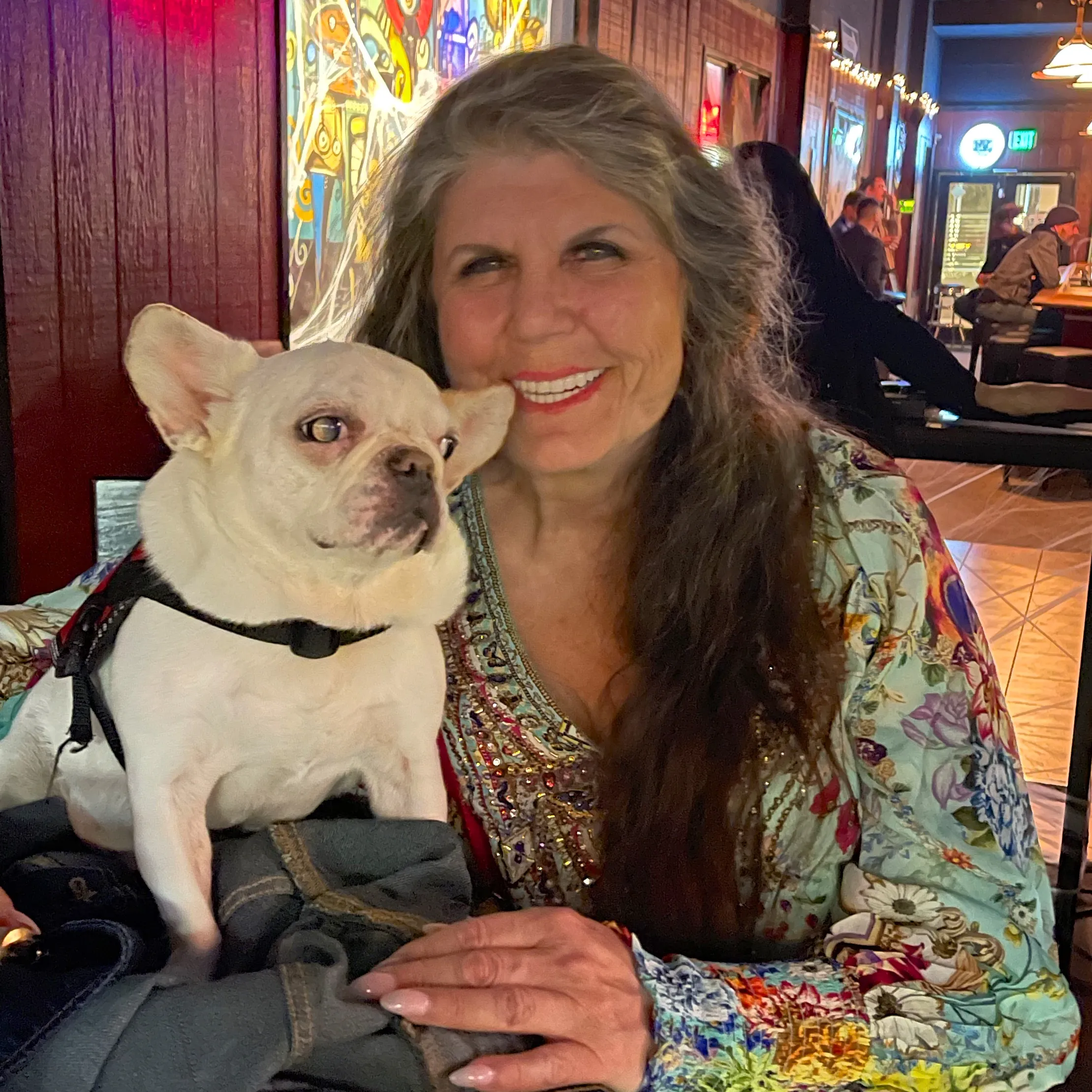 Anahata Graceland sitting in a restaurant with her calm Micro Mini Royal Frenchel service dog.