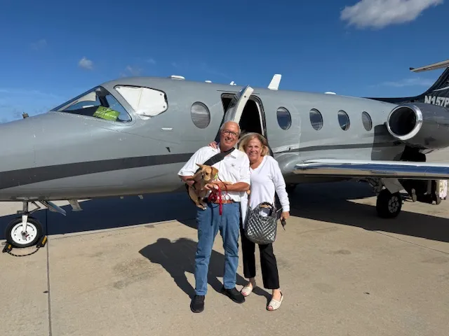 Micro Mini Royal Frenchel traveling with a couple near a private airplane.