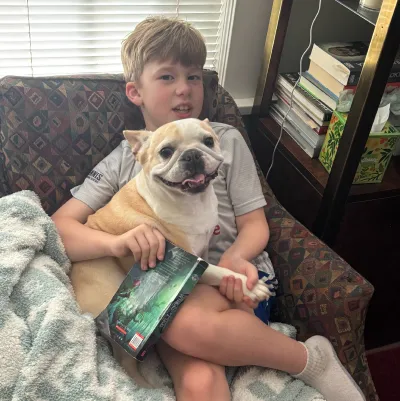 Small Royal Frenchel snuggling with a child on a couch.