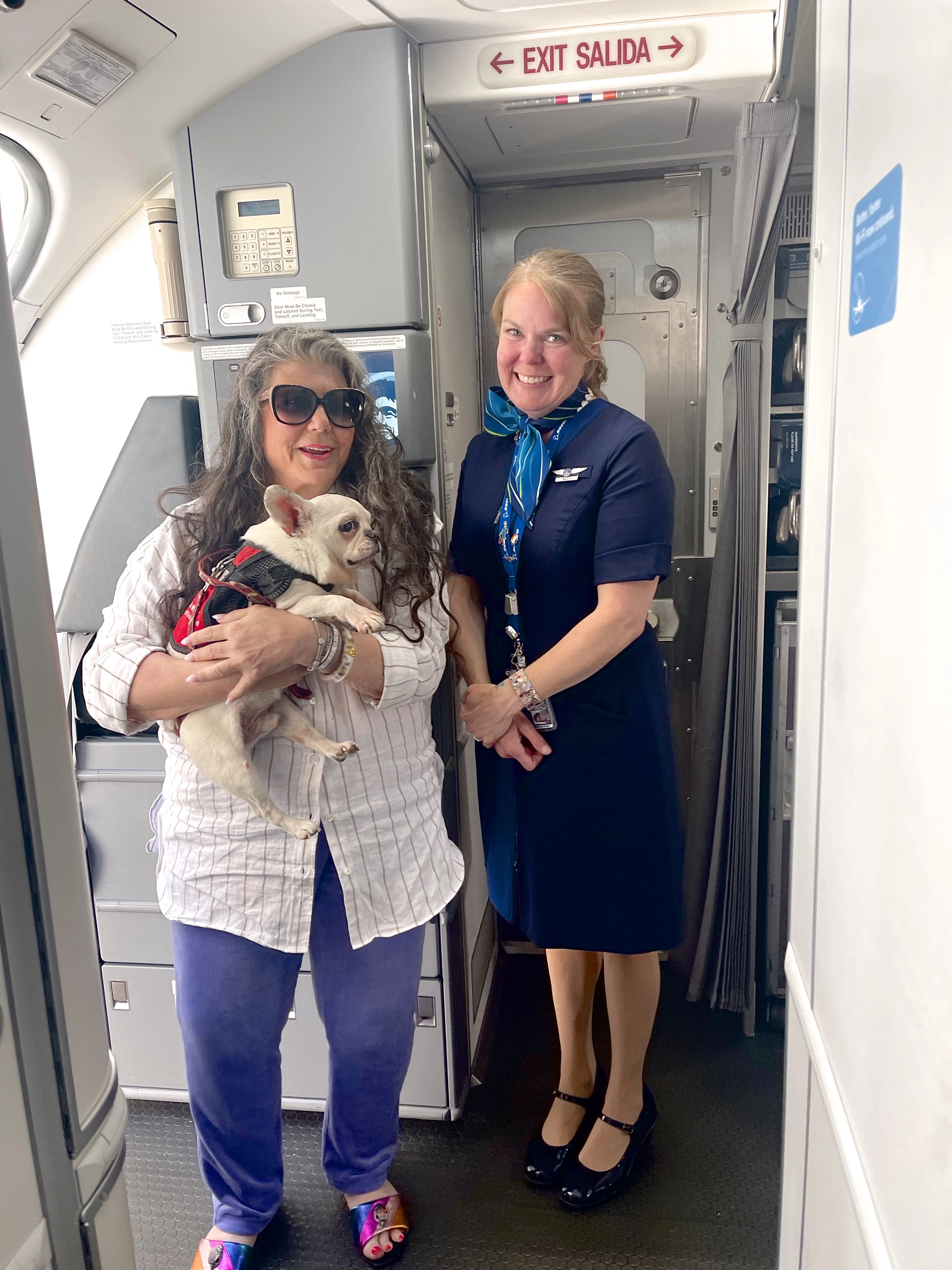  Anahata Graceland standing on a plane with her Royal Frenchel service dog and a flight attendant.