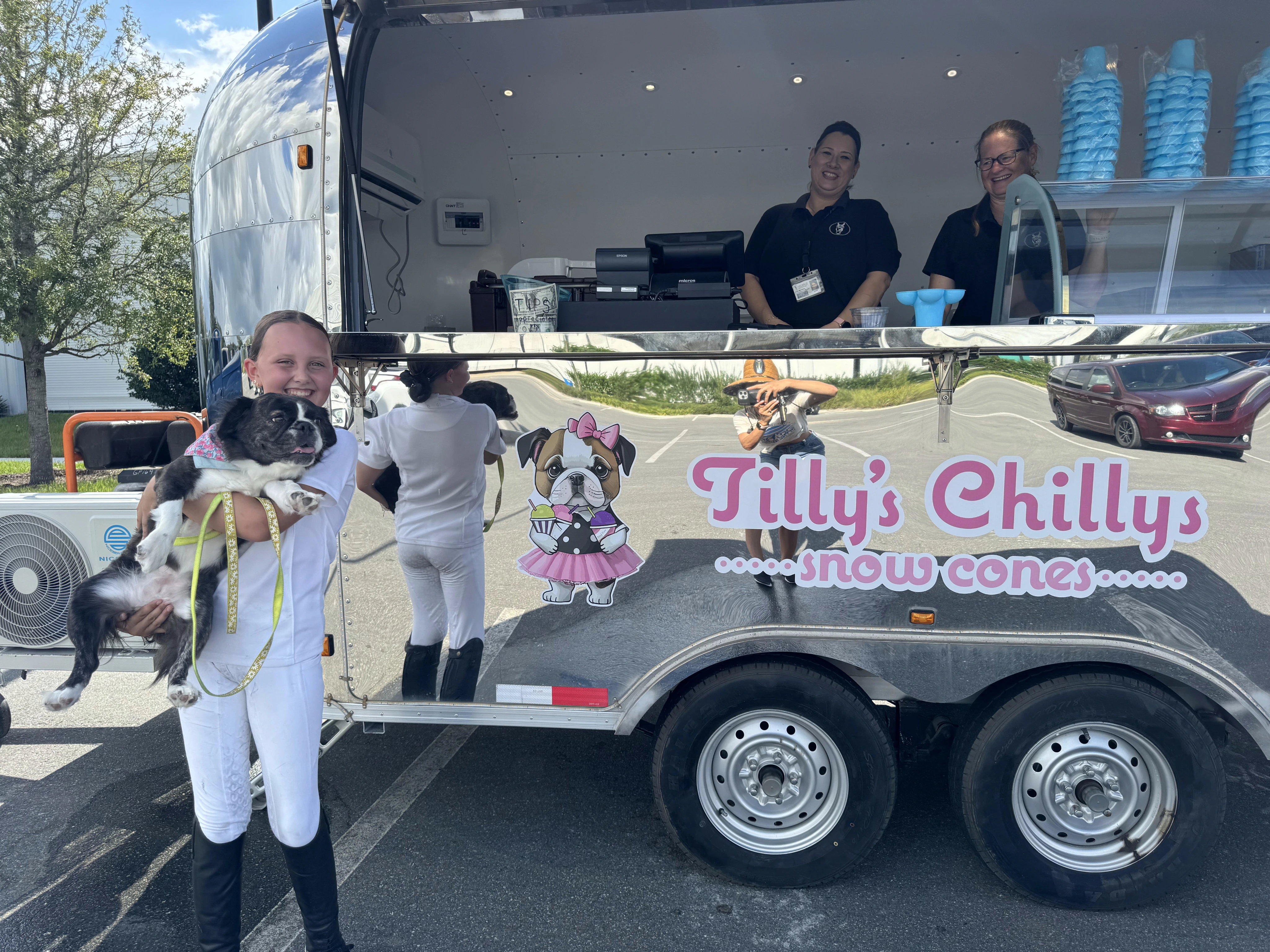 Girl holding her Royal Frenchel outside by a snow cone truck.