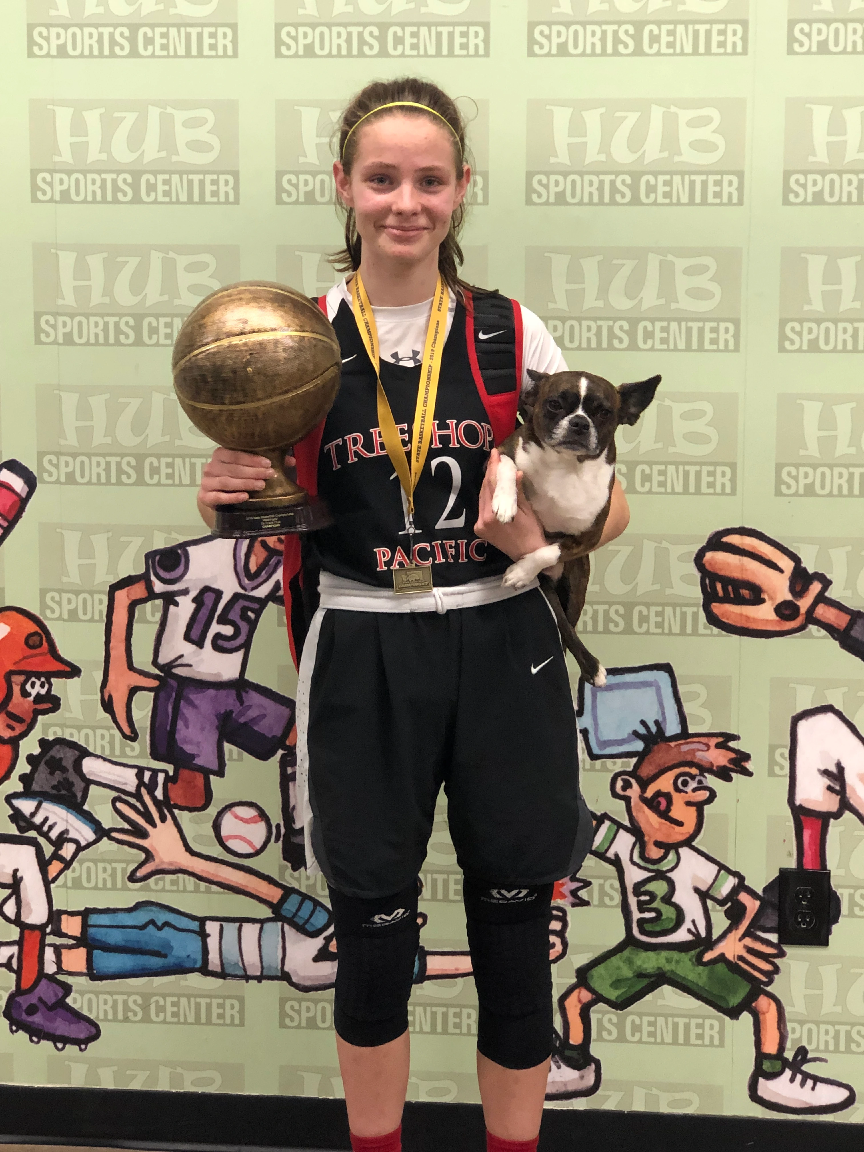 Girl holding a basketball trophy and her Royal Frenchel after a game.