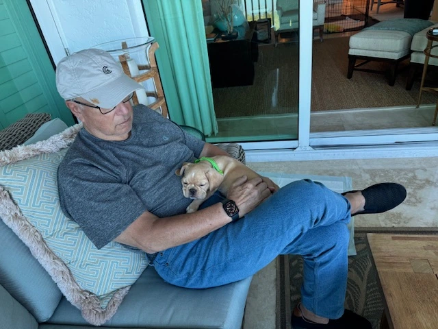 Man sitting outside on a couch with his Royal Frenchel on his lap.