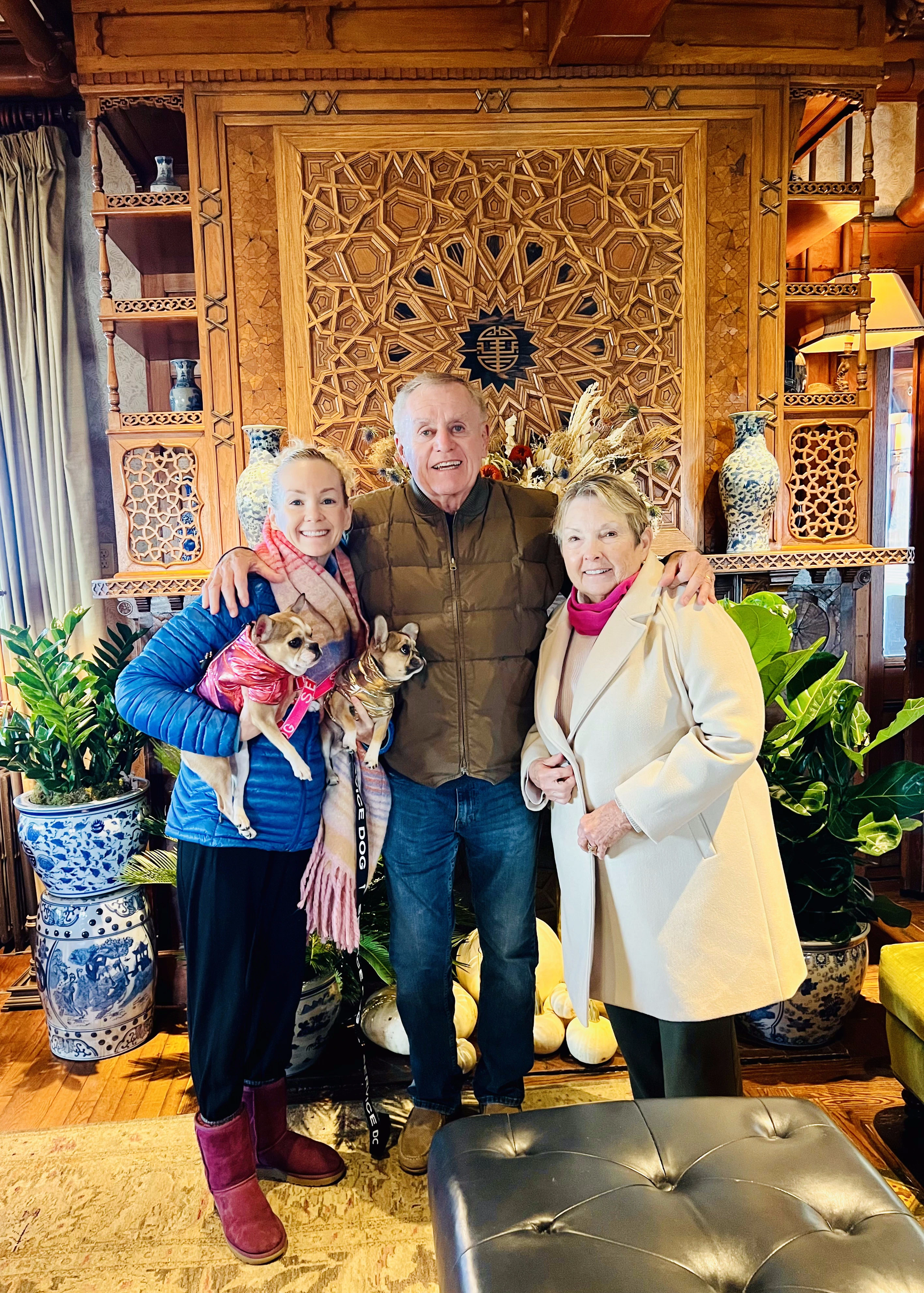 Two Royal Frenchels being held in a living room with family nearby.