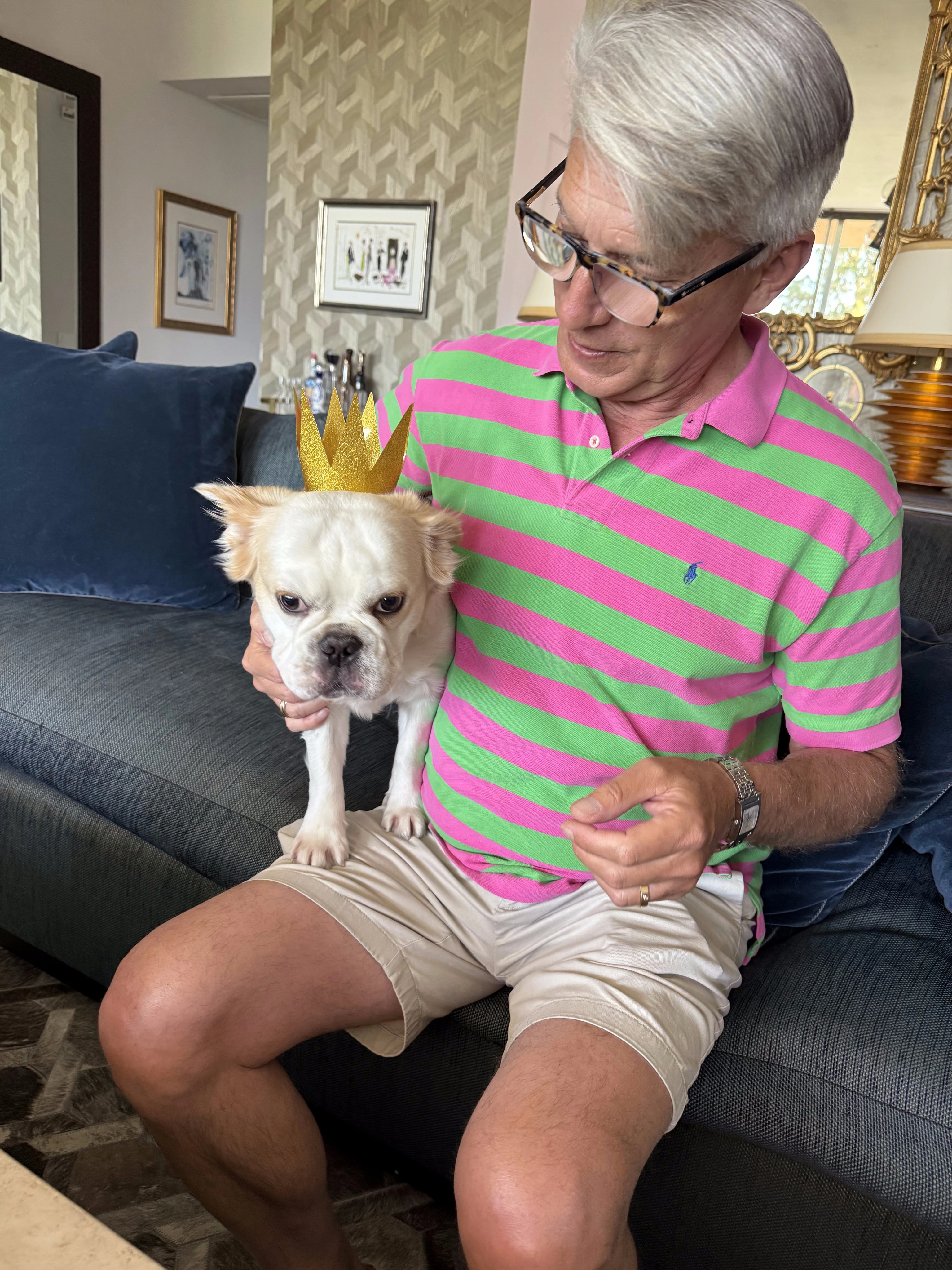 Man sitting on a couch with his Royal Frenchel wearing a small crown.