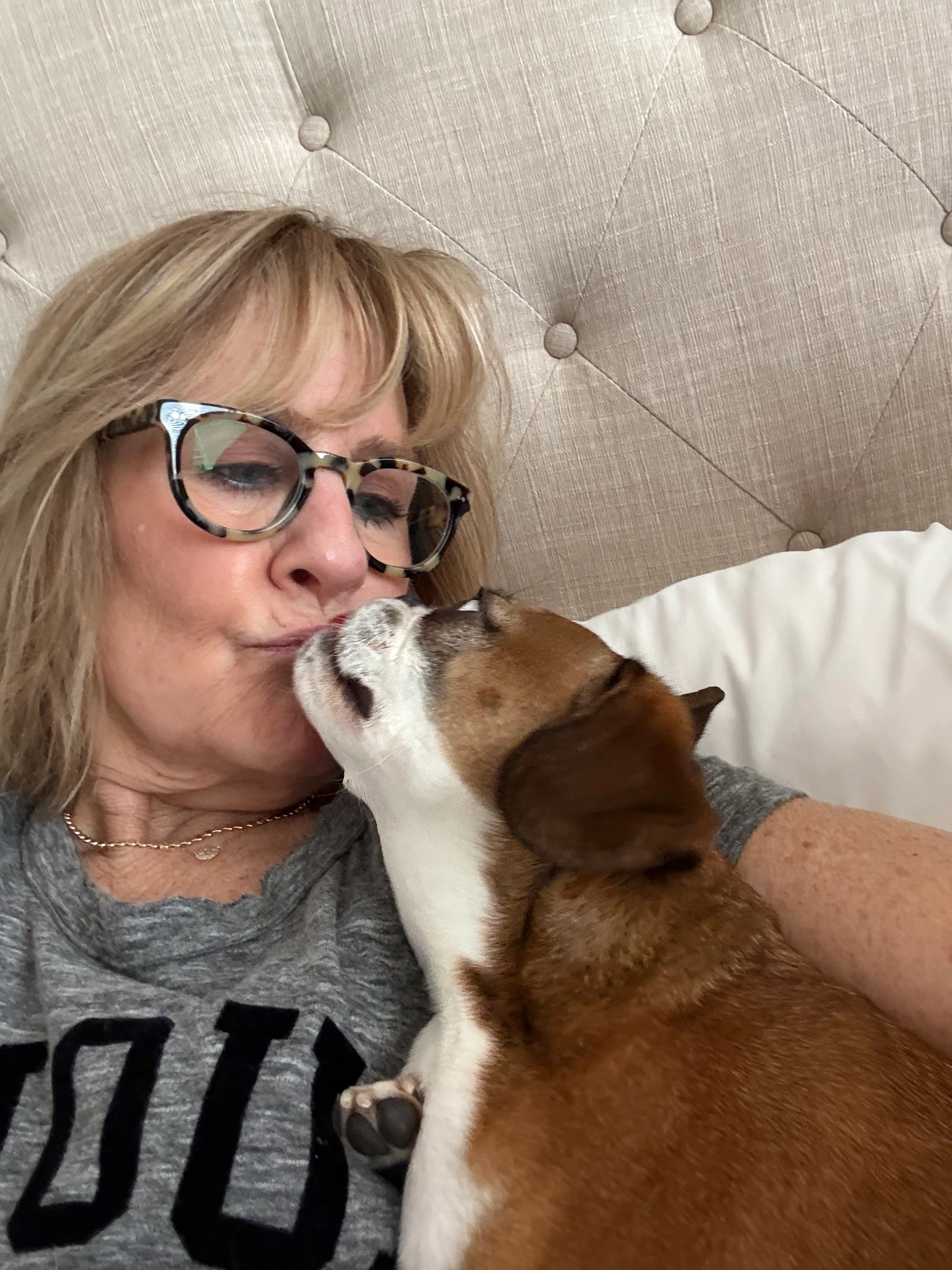 Woman snuggling in bed and kissing her Royal Frenchel puppy.