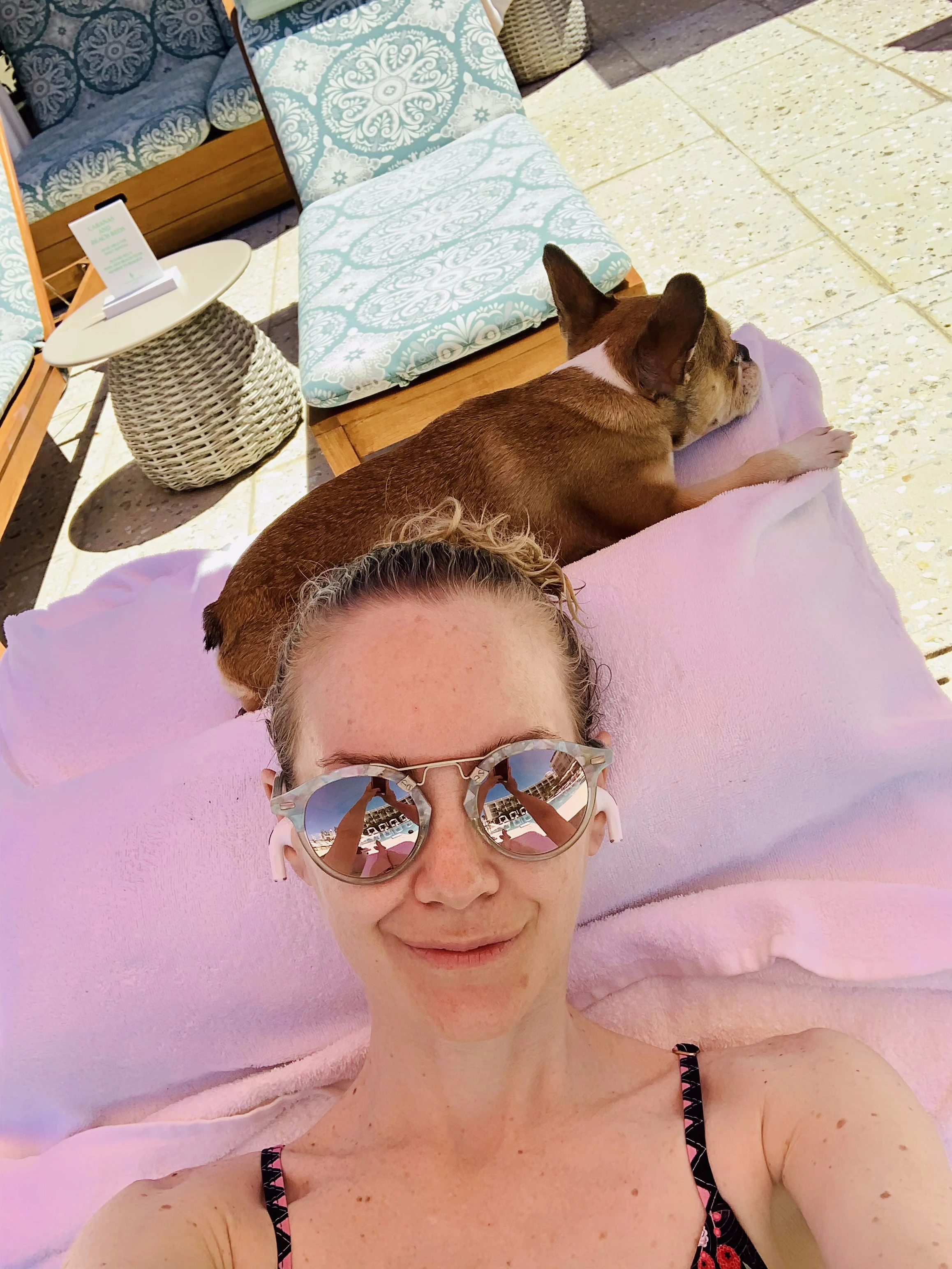 Woman relaxing on a tanning bed with her Royal Frenchel beside her.