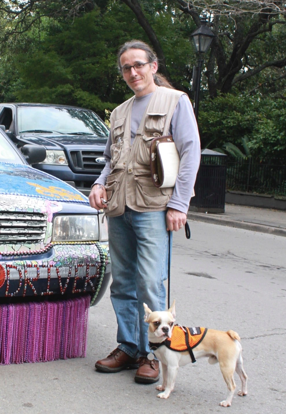 Man standing on a city street with his Royal Frenchel service dog by a car.