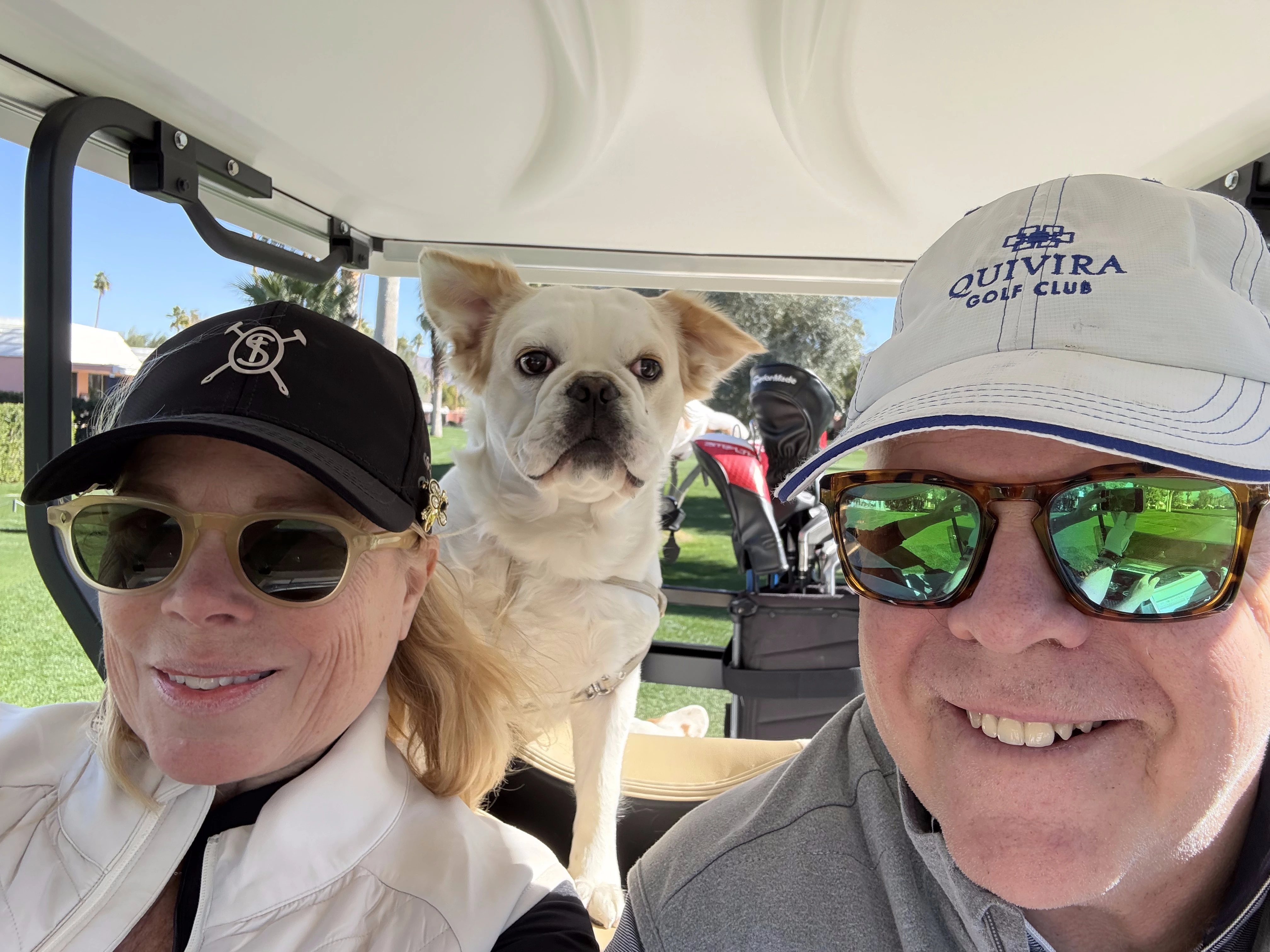 Couple riding in a golf cart with their Royal Frenchel in the back.