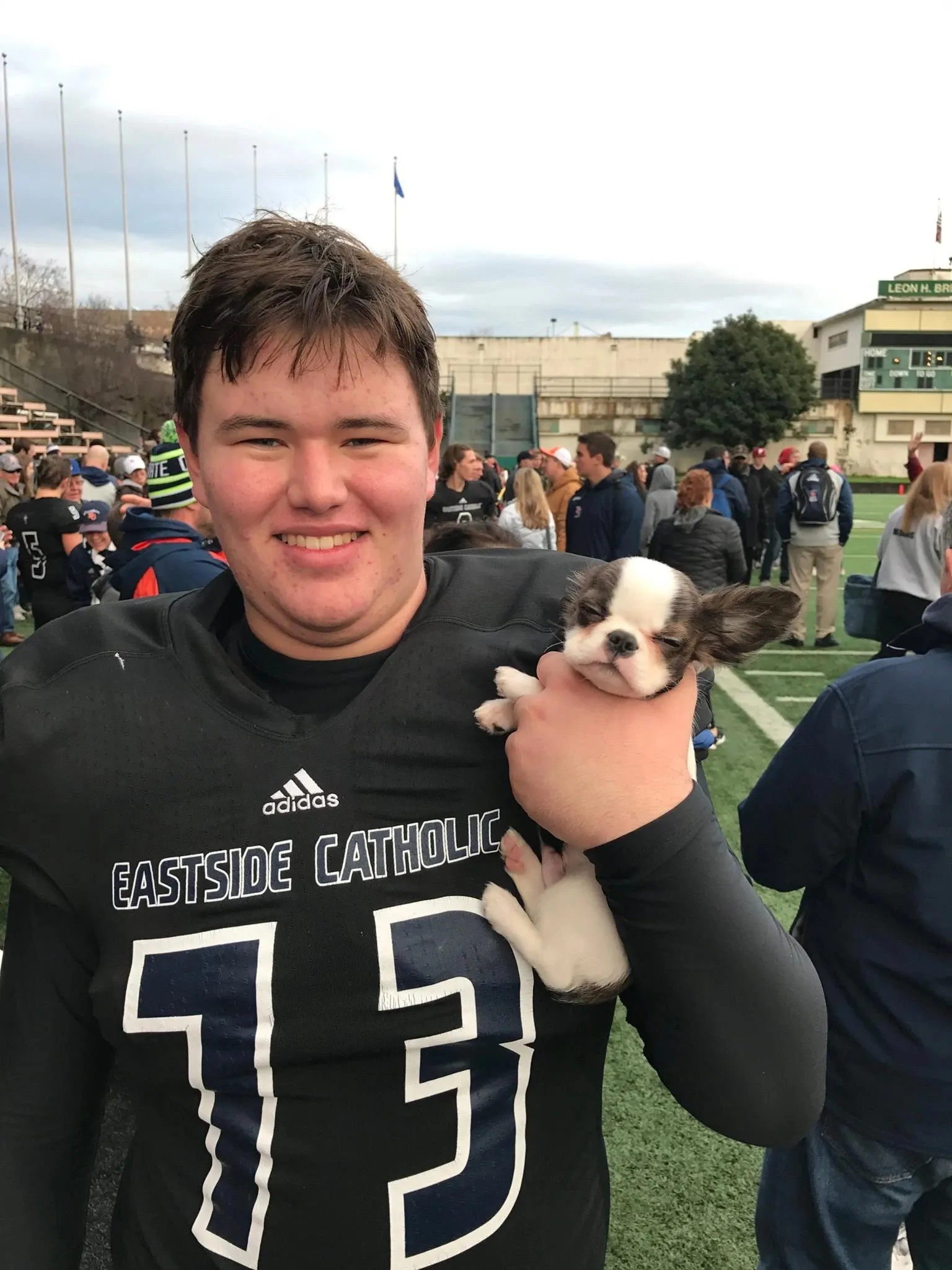 Football player holding a small Royal Frenchel puppy outdoors.