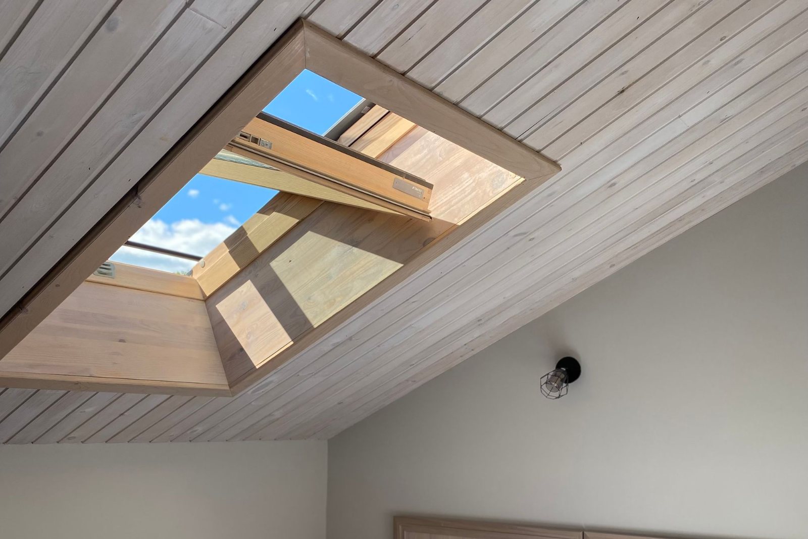 Chambre sous les combles, lit installé sous une fenêtre de toit ouverte sur le ciel — pose de Velux à Betton par Avenir Eco Couverture