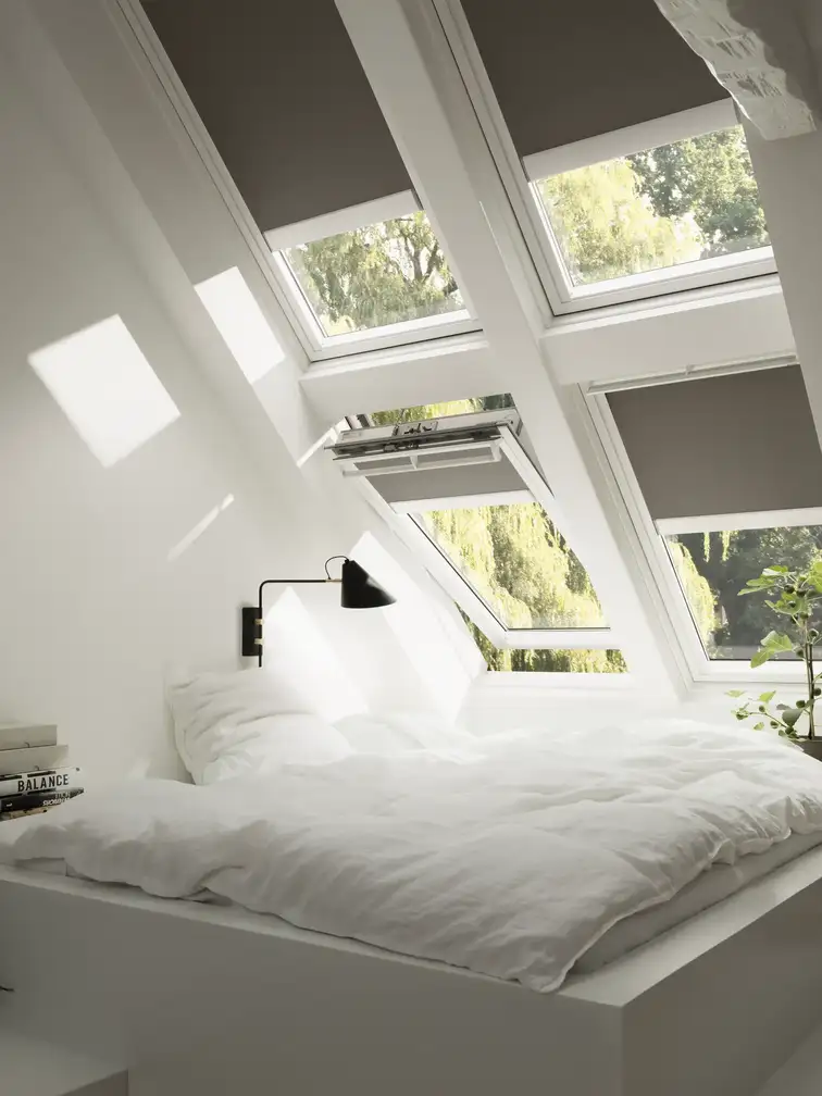 Deux combinaisons de trois fenêtres de toit VELUX ouvertes sur la campagne depuis les combles à Melesse