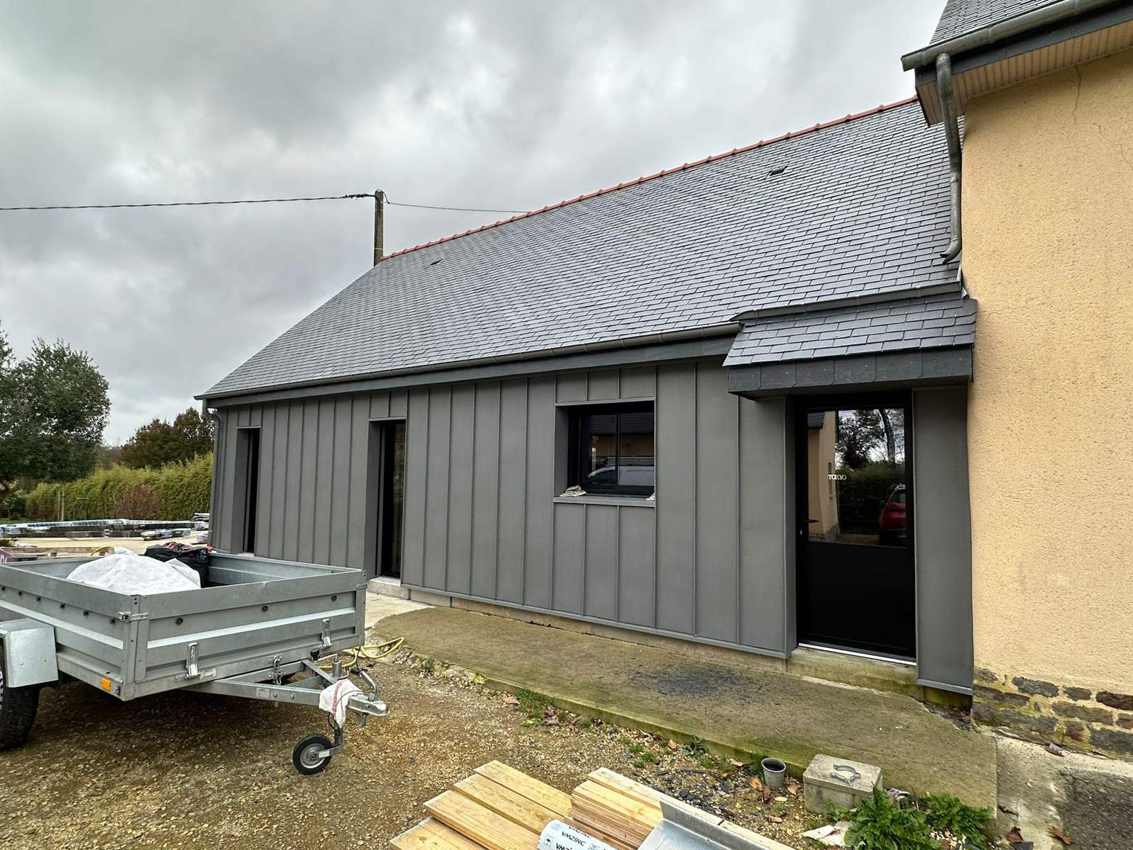 Auvent d'entrée couvert en ardoise et bardage zinc quartz de l'agrandissement à La Mézière