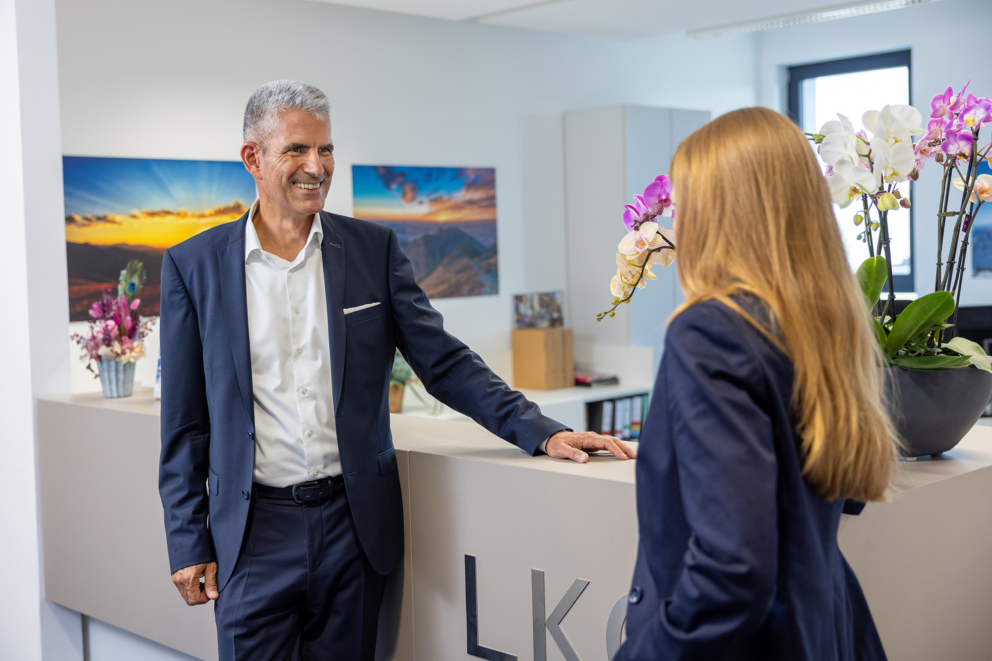 Zwei Personen in Businesskleidung begrüßen sich in einem modernen Büroeingansgbereich.