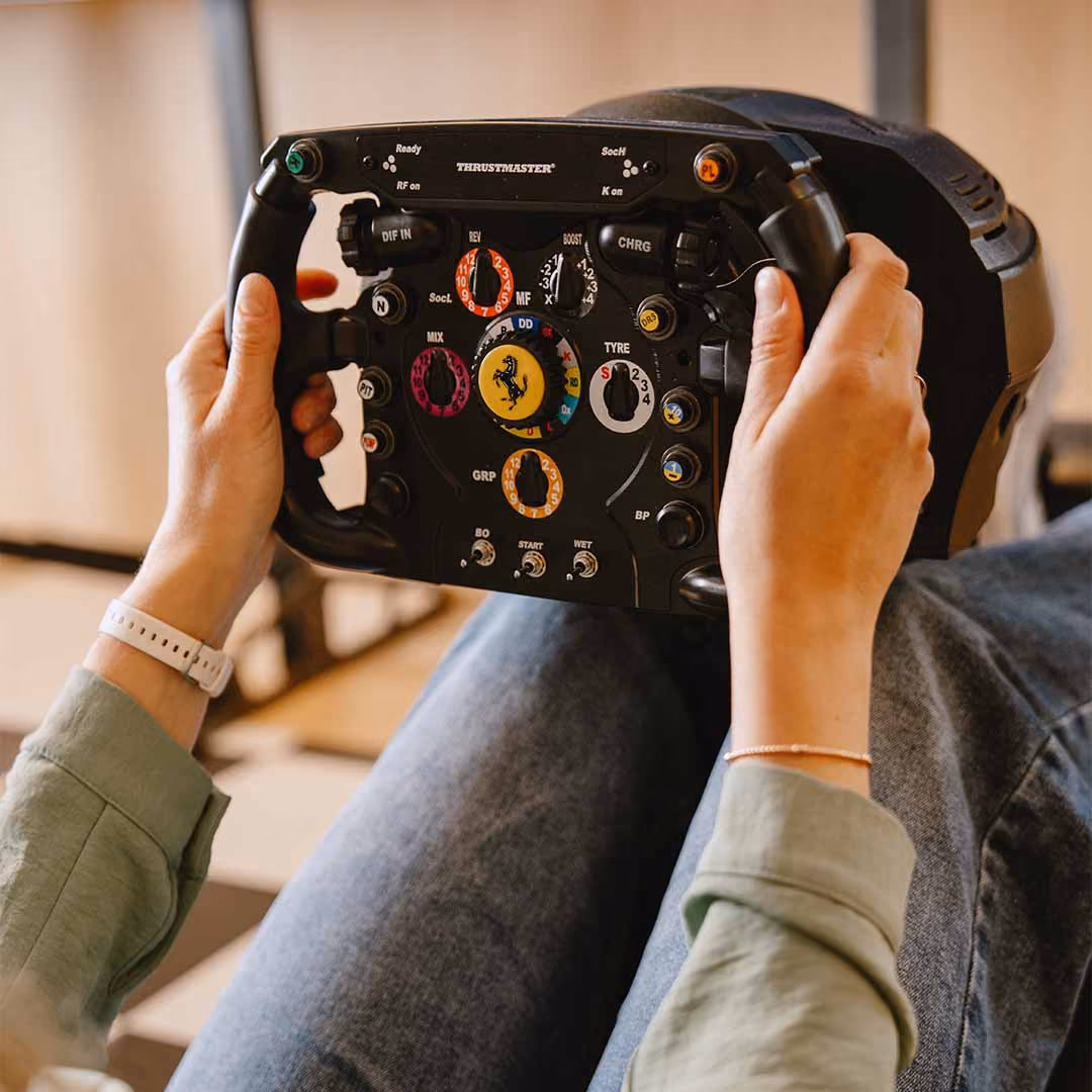 Persoon houdt een Thrustmaster racestuur met Ferrari-logo en meerdere knoppen vast.