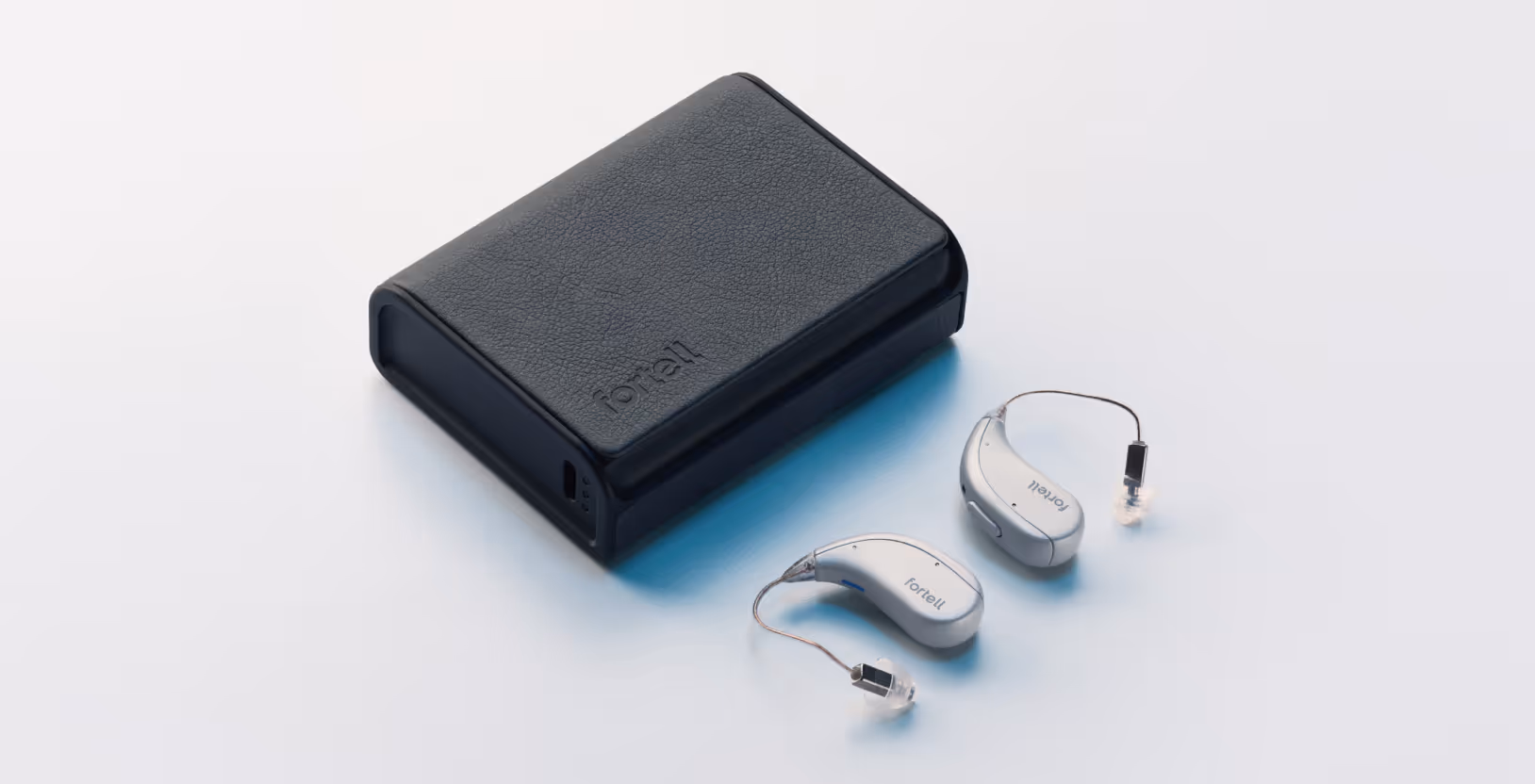 Pair of silver behind-the-ear hearing aids with clear wires next to a black leather charging case.