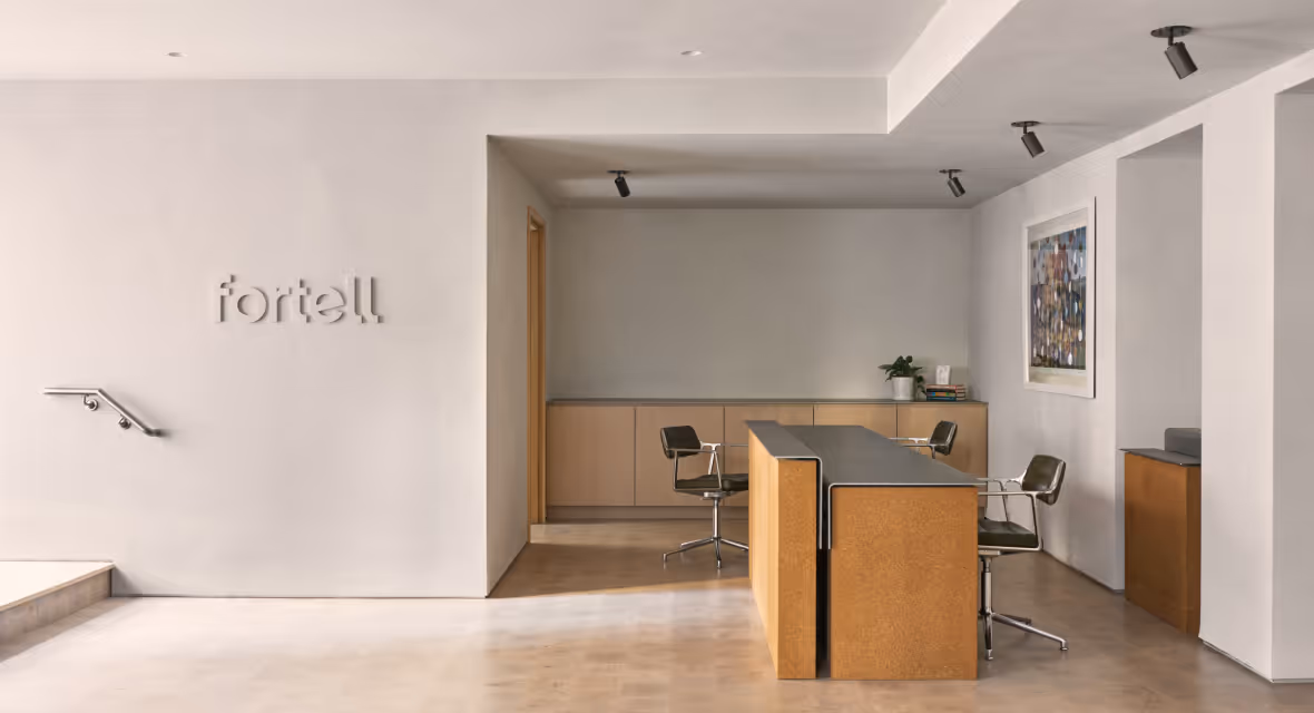 Minimalist office lobby with a wooden reception desk, three black swivel chairs, cabinetry in the back, and a Fortell sign on the white wall.