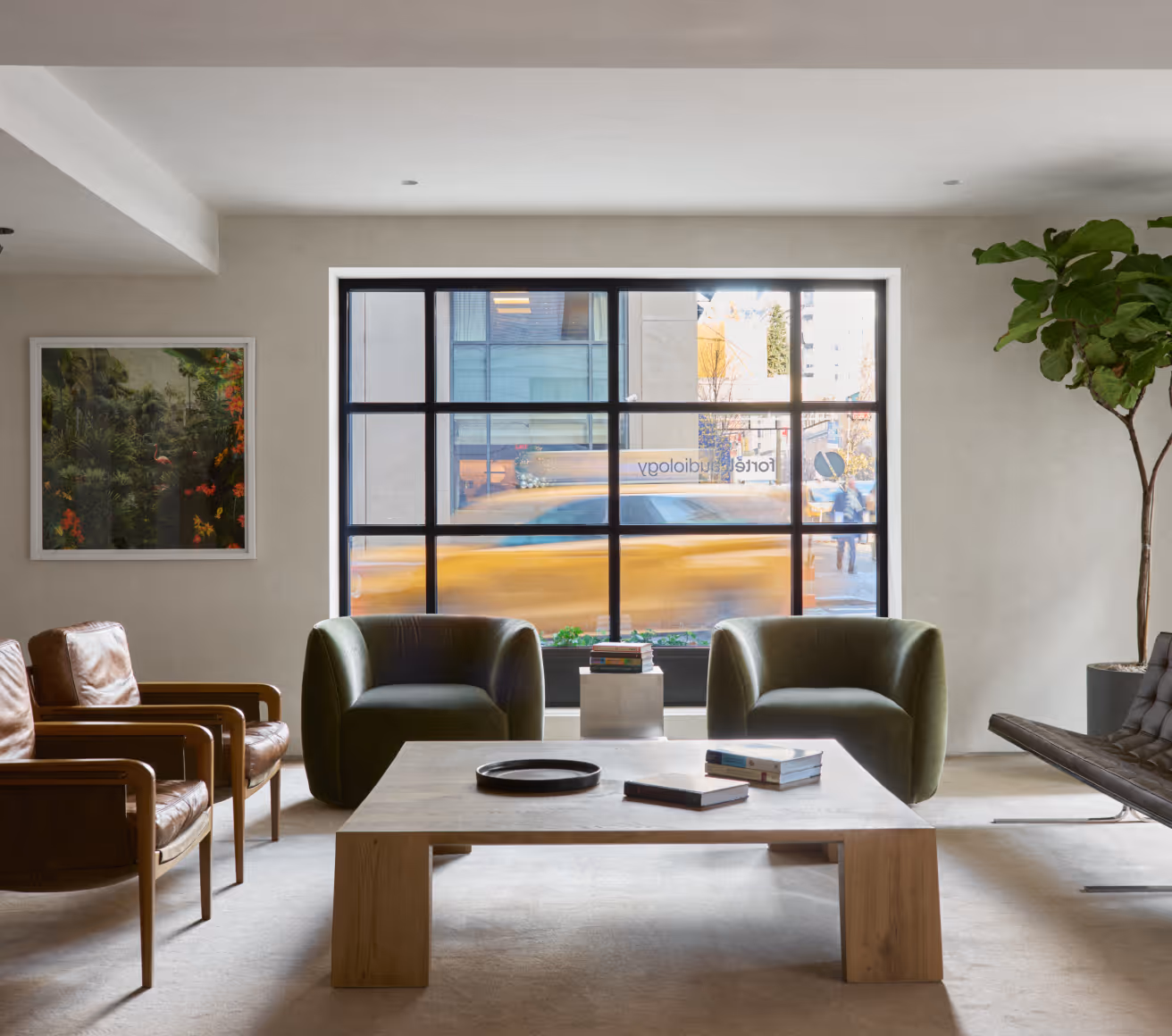 Modern waiting room with leather and green armchairs, wooden coffee table with books, large window showing blurred yellow taxi outside.