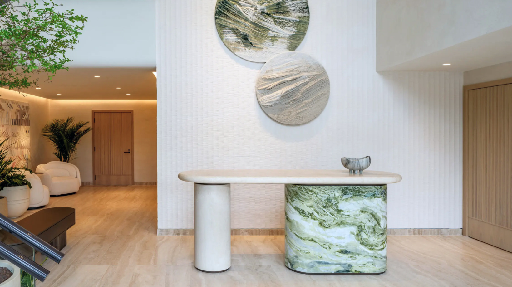Modern interior with beige marble floor, sculptural table, round wall art, and cozy seating area.