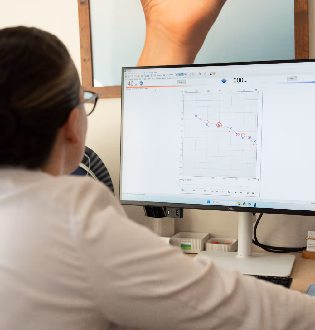 Person with glasses viewing an audiogram showing hearing test results on a computer screen.