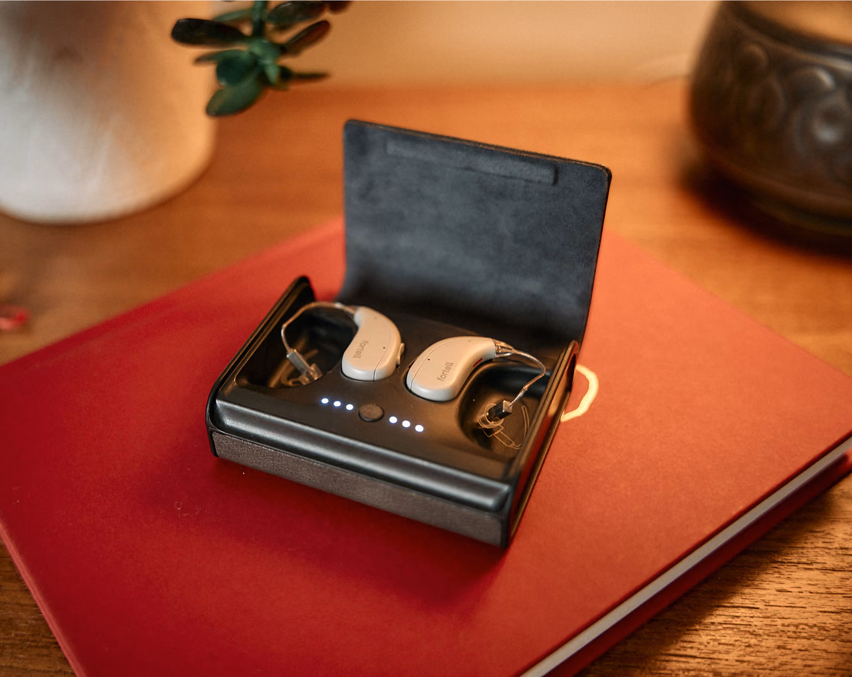Pair of Silver Fortell hearing aids in their open charging case on a red book.