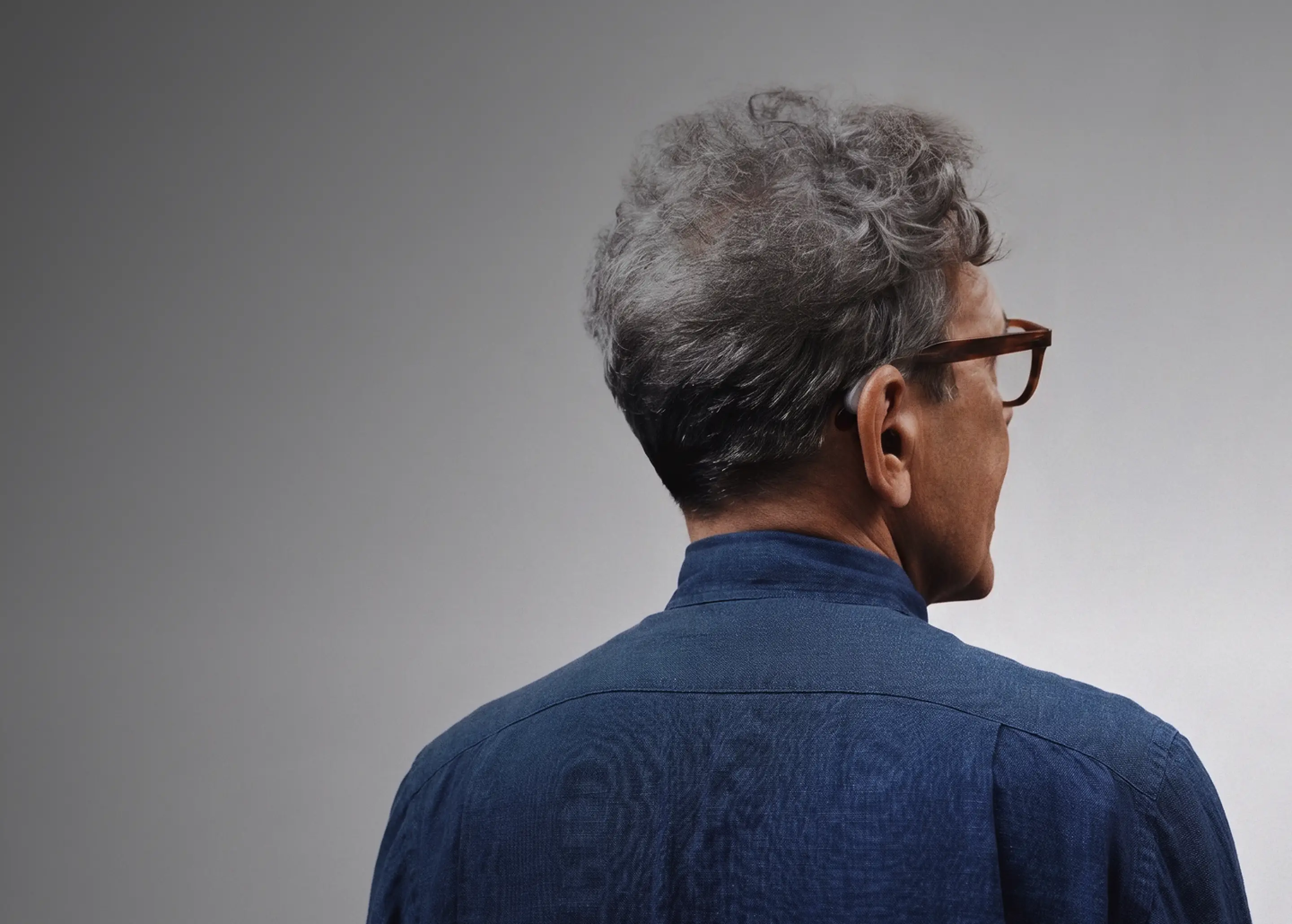 Man in glasses wearing a Fortell hearing aid behind the ear, seen from behind