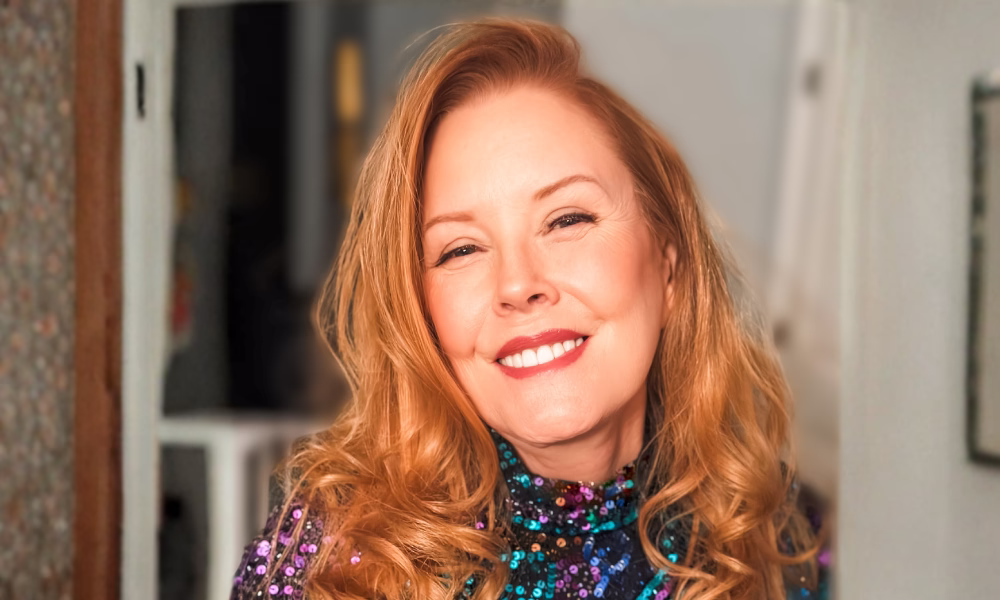 Smiling woman with long red hair wearing a sequined top.