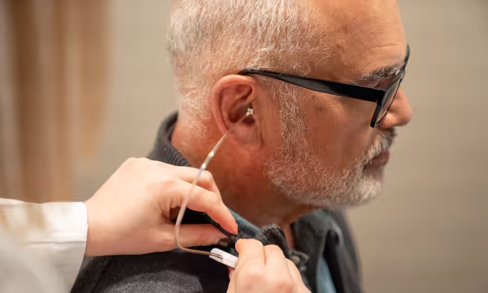 Audiologist placing a thin tube in an older man's ear during a hearing aid fitting.