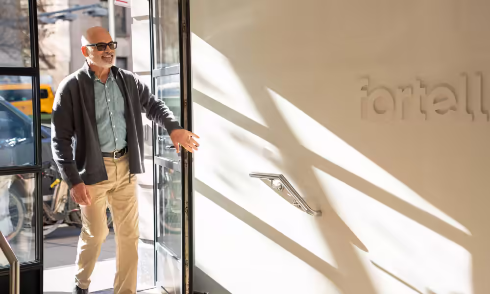 Smiling older man in glasses walks through the sunlit entrance of a Fortell clinic.