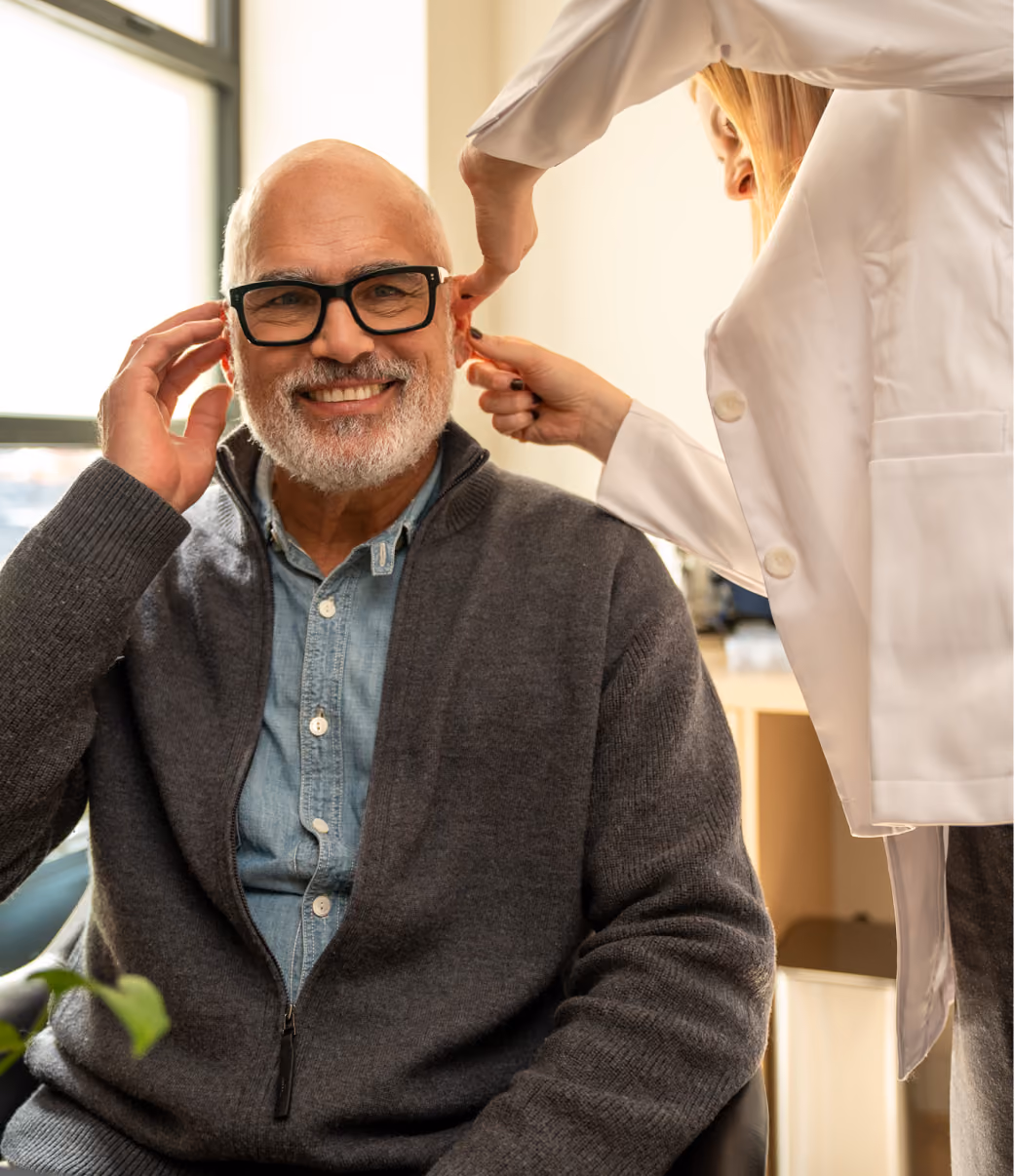 Audiologist helping a smiling patient fit a hearing aid