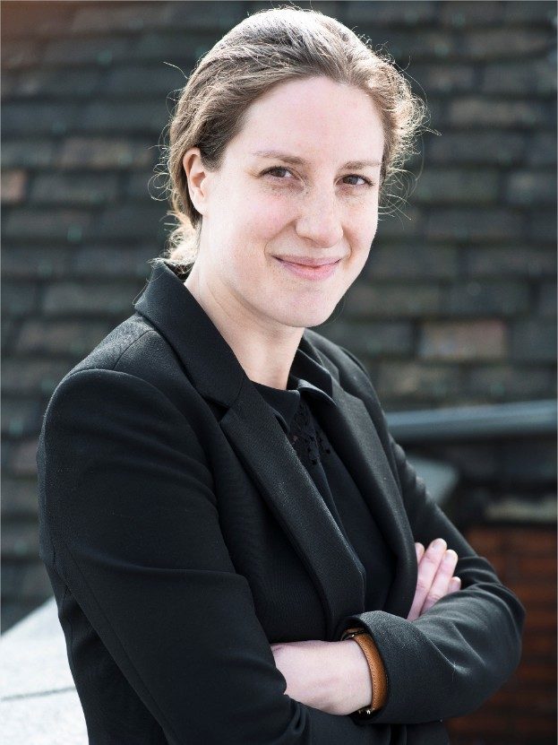 Portrait de Clémense Moullot, en veste noir, souriante avec les bras croisés. 
