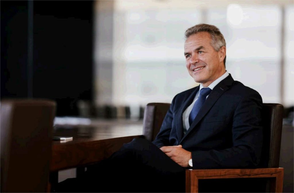 Eric Borremans, assis sur un fauteuil. Il porte un costume et une cravate. 