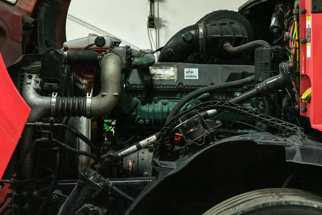 Heavy-duty engine with intake piping, hoses, wiring, and cooling components exposed inside a red truck cab.