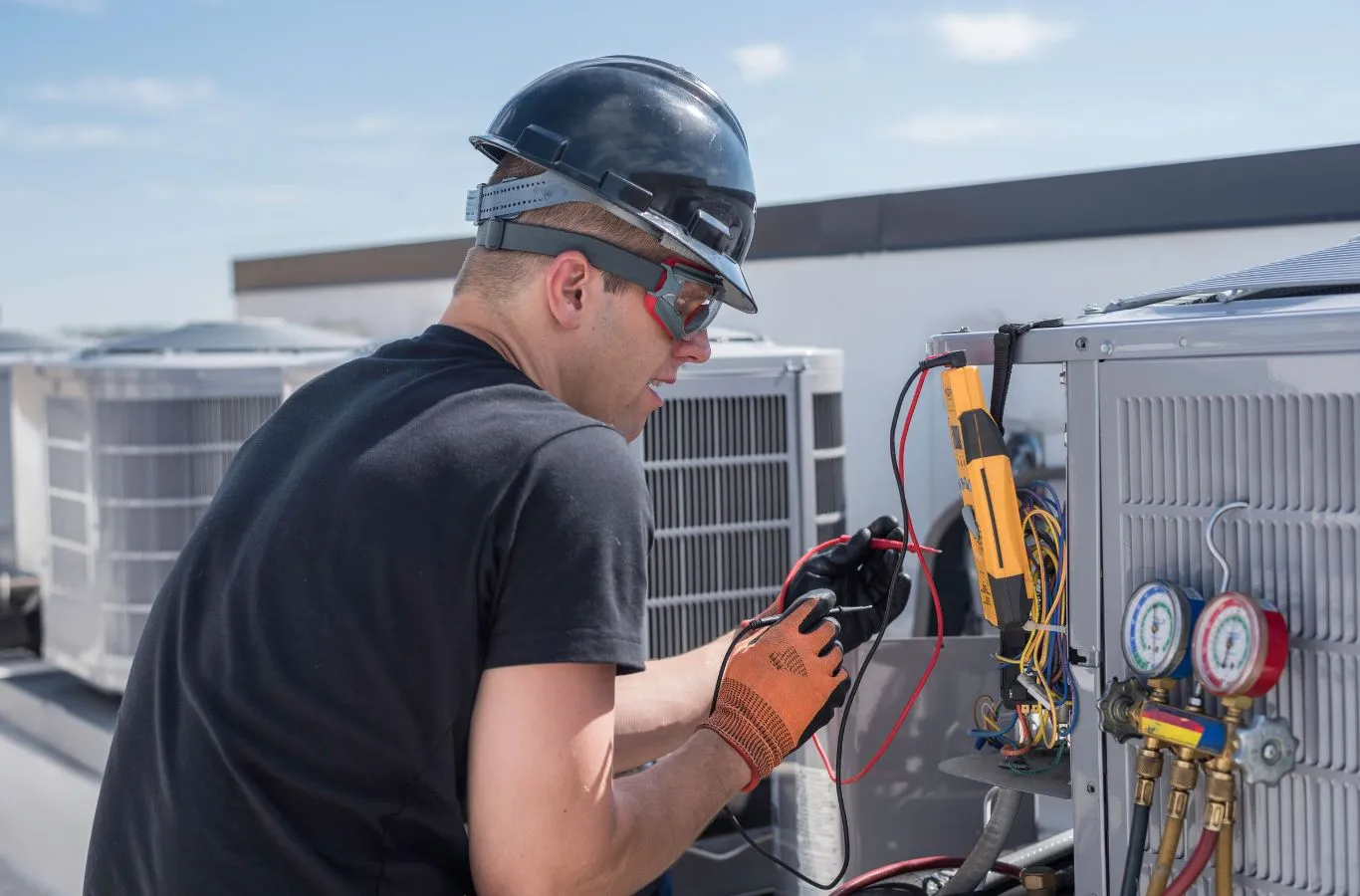 HVAC technician using a multimeter and refrigerant gauges on a rooftop unit during HVAC service in Hillsborough County, FL.